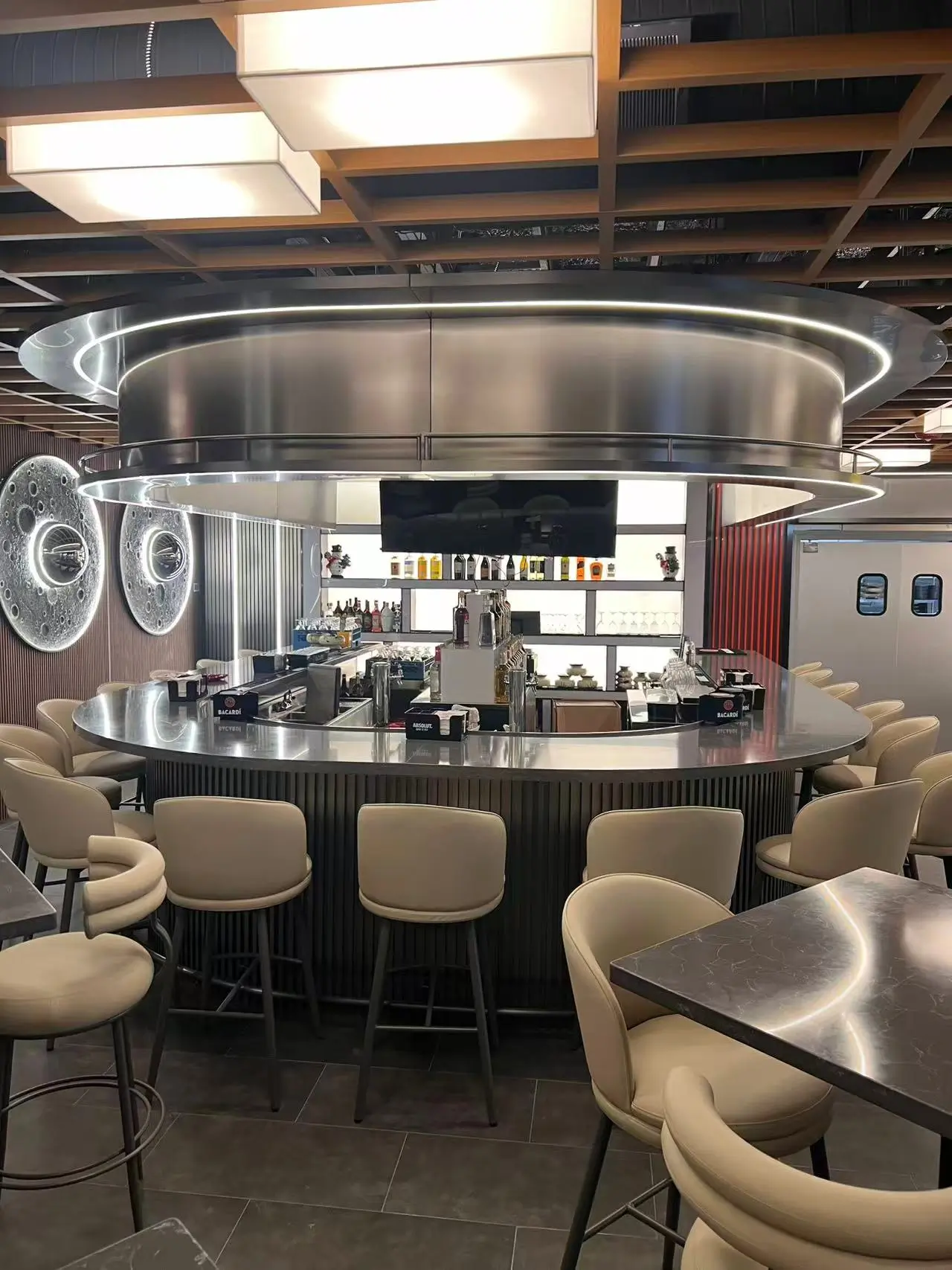 Interior view of the circular bar area at Imperial Dynasty Chinese Restaurant in Cranston, featuring polished metallic surfaces, soft beige seating, recessed LED lighting, and decorative moon-themed wall mirrors.